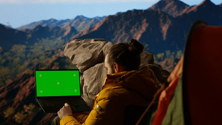 Young traveler embraces high altitude wilderness next to chroma key, using a device where the crisp...