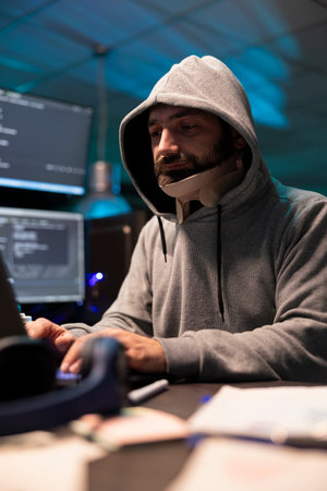 Hooded injured man working diligently on cybersecurity, analyzing networks and spyware risks....