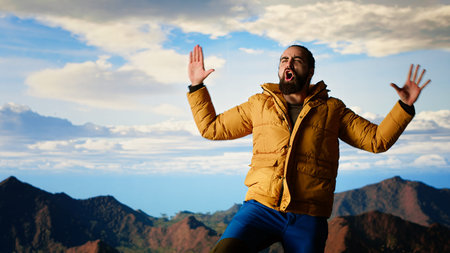 Happy climber cheering and feeling pleased while he stretches arms toward the sky, feeling the...