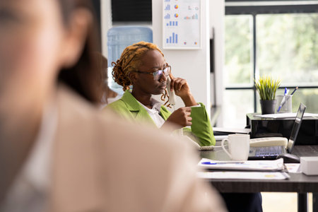 Black manager speaks on landline phone with internal employee, offering guidance and providing...