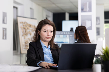 Focused white woman works on laptop, creating reports and planning schedules for upcoming...