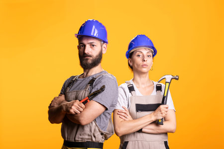 Caucasian builders pose in overalls with arms crossed expressing readiness for repair tasks. Team of...