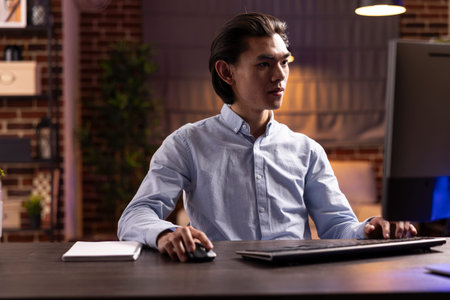 Asian man works remotely during evening hours, researching strategies and improving plans for small...
