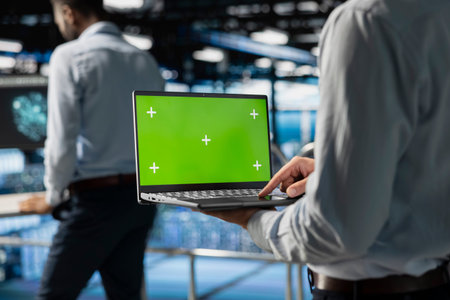 Data center staff using green screen mockup on laptop screen, doing maintenance on server rigs...