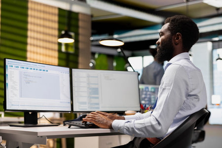 Software developer reviewing code snippets in modern workplace, adjusting configurations. African...