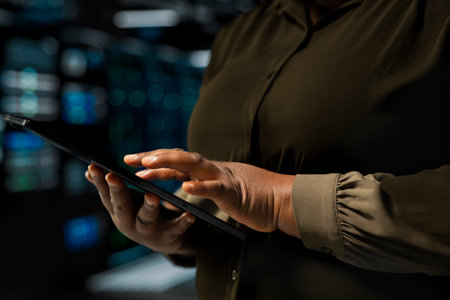 Close up of admin holding tablet walking through server room rows lined with storage hardware. IT...