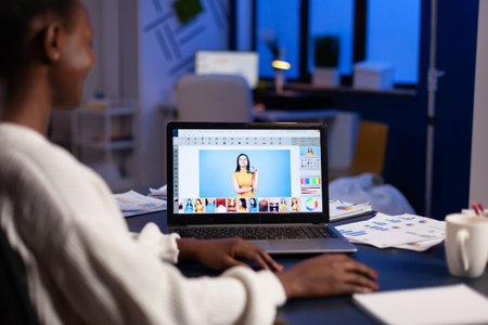 Dark skin freelancer retoucher woman working overtime on laptop with photo editing software....