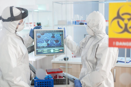 Team of scientist looking at virus evolution standing in lab danger zone dressed in ppe suit. Group...