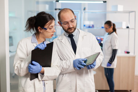 Group of medical researchers discussing about vaccine development, standing in equipped lab pointing...
