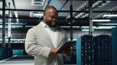 Smiling admin using tablet in in data center maintaining infrastructure for workloads. Joyful IT...