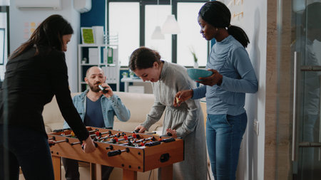 Multi ethnic coworkers playing foosball game at table for entertainment after work. Team of...