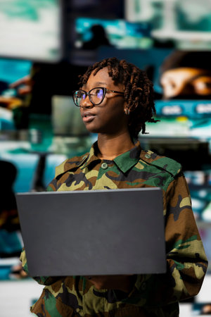 Soldier wearing camo uniform operating on high tech equipment using notebook. Military officer using...
