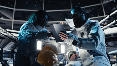 Astronaut reviewing onboard analytics on tablet, talking to colleague during space mission....