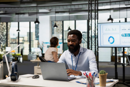 African american male employee focused in project planning in corporate workspace, reading online...
