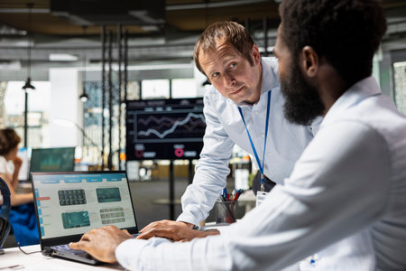 Caucasian male executive standing and inquiring of financial data from african american employee at...