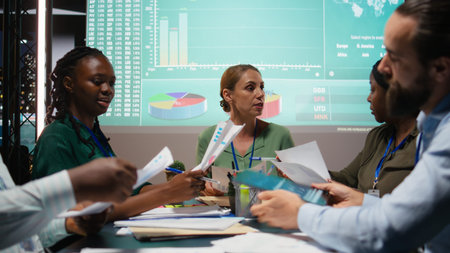 Close up of diverse staff hand over data projections papers in a meeting after hours for...