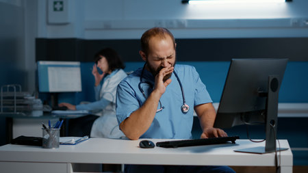 Tired stressed physician nurse working over hours at medical expertise in hospital office, typing...