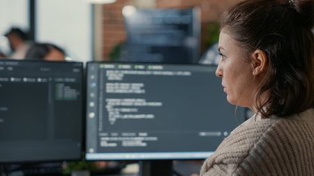 Over shoulder view of focused database designer writing code looking at multiple computer screens...