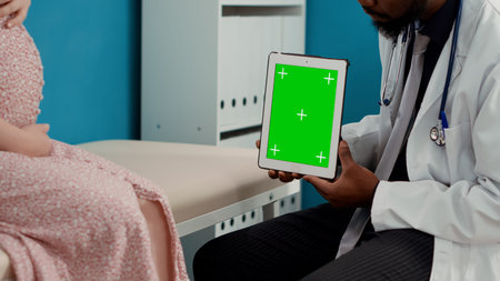 Male medic working with greenscreen on tablet at examination, consulting pregnant person. Doctor...