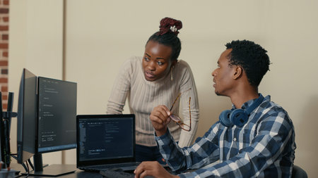 Database developer removing glasses while explaining algorithm to colleague coder pointing at...