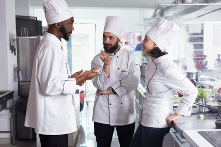 Culinary experts focus on cooking new dishes in a modern kitchen, wearing chef hats and uniforms....