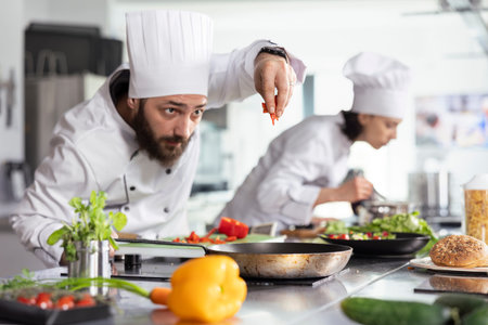 Gastronomy expert in uniform adding cut bell pepper for a gourmet dish with fresh produce, creating...