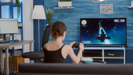 Gamer girl holding wireless controller playing console video game first person shooter on tv while...