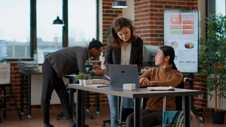 Woman with disability talking to colleague about business charts development to create strategy for...