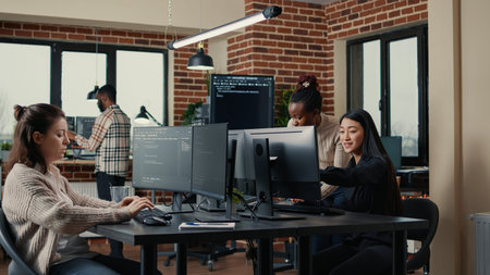 Software engineer typing source code on computer keyboard while colleagues sit down at desk for...
