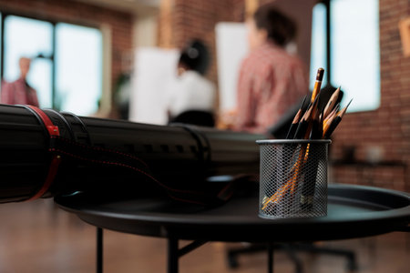 Pencils in metal holder and canvas tube on table in modern art studio, drawing tools and supplies in...