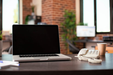Empty startup office with open laptop, telephone, papers and coffee cup neatly placed on desk....