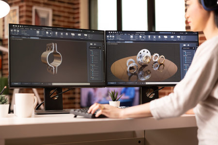 Female engineer reviewing mechanical clamp and gear prototype on dual monitors using CAD software....
