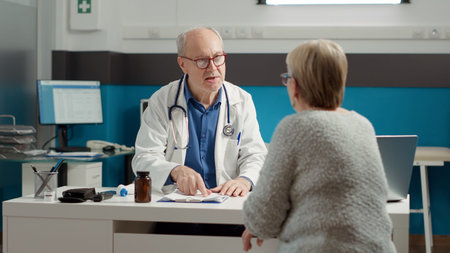 Senior physician doing checkup consultation with retired sick patient in medical office, talking...
