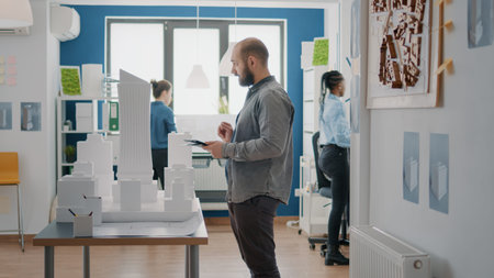 Architect using digital tablet and building model to design blueprints plans for construction. Man...