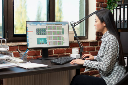 Woman researcher carefully reviewing market data on her computer in modern workspace. Young female...