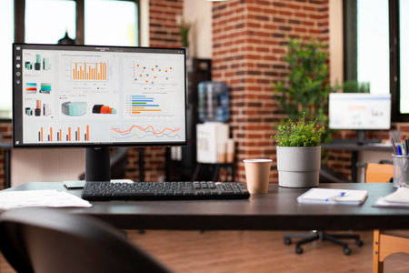 Desktop monitor displaying stock market charts and company growth data is set on desk in vacant...
