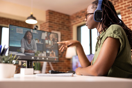 Young black woman sitting at desk in home office, engaging in online discussions with coworkers on...