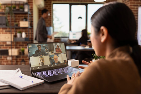 Asian businesswoman attending a virtual meeting on laptop with her remote coworkers, discussing...