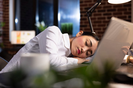 Overworked corporate manager sleeping at her office desk, taking a break during her night shift. Her...
