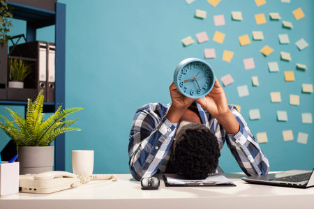 Exhausted male manager resting his head on table and carrying an analogue clock, counting down to...
