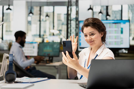 Caucasian woman waves at phone, greeting colleague on video call to start online conversation in...