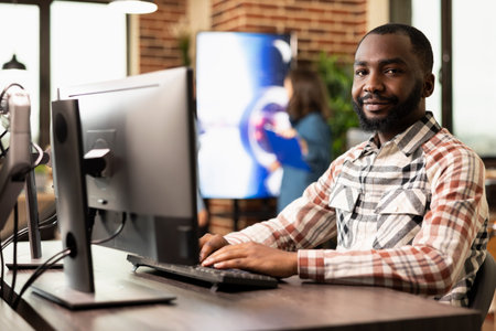 Confident businessman sitting with desktop pc on his desk, posing for camera in brick wall office....