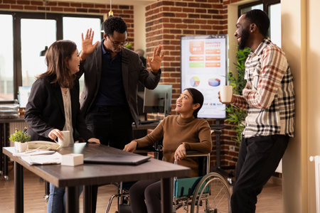 Asian woman in wheelchair surrounded by her diverse coworkers, taking a short break and having a...