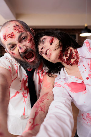 Workers having fun at work dressed as zombies for Halloween, taking selfies while growling and...