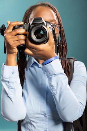 Young black woman raises her DSLR, eyes focused, capturing a moment with calm intensity. Female...