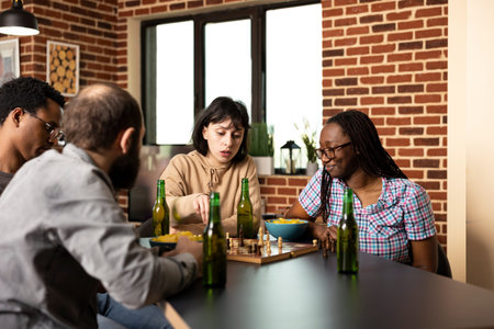 Multiethnic people sitting at table and enjoying chess match in brick wall room. Caucasian woman...