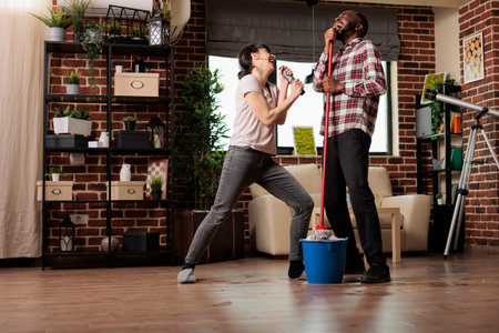 Happy multiracial couple singing with emotion, enjoying housework together. Woman singing with...