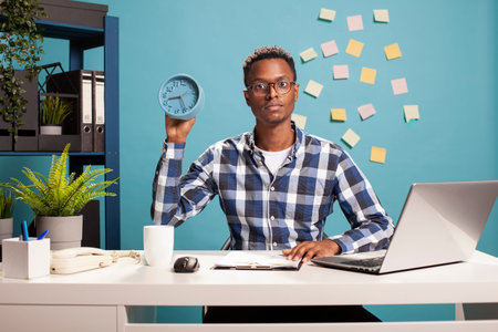 Portrait of a young African American freelancer sitting at office desk with a clipboard and showing...