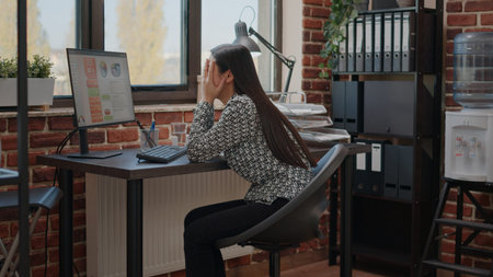 Overworked woman feeling stressed about work deadline, working on computer in startup office....