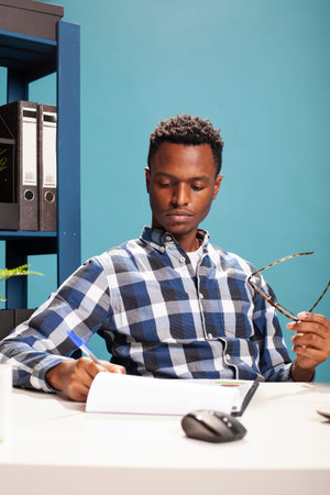 Portrait of a black man holding his spectacles and reviewing paperwork at his desk. African american...